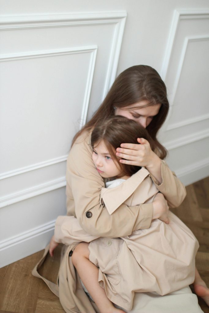 A mother lovingly embraces her child in an intimate indoor setting, portraying a scene of warmth and care.
