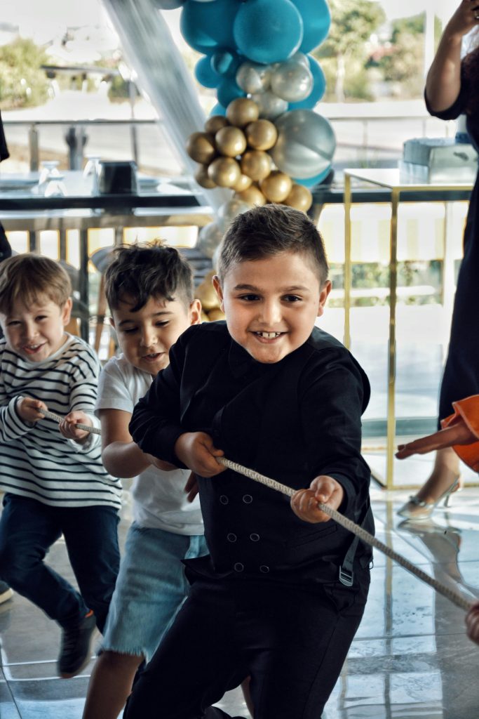 Group of smiling kids playing tug of war during an indoor birthday party with colorful decorations.
