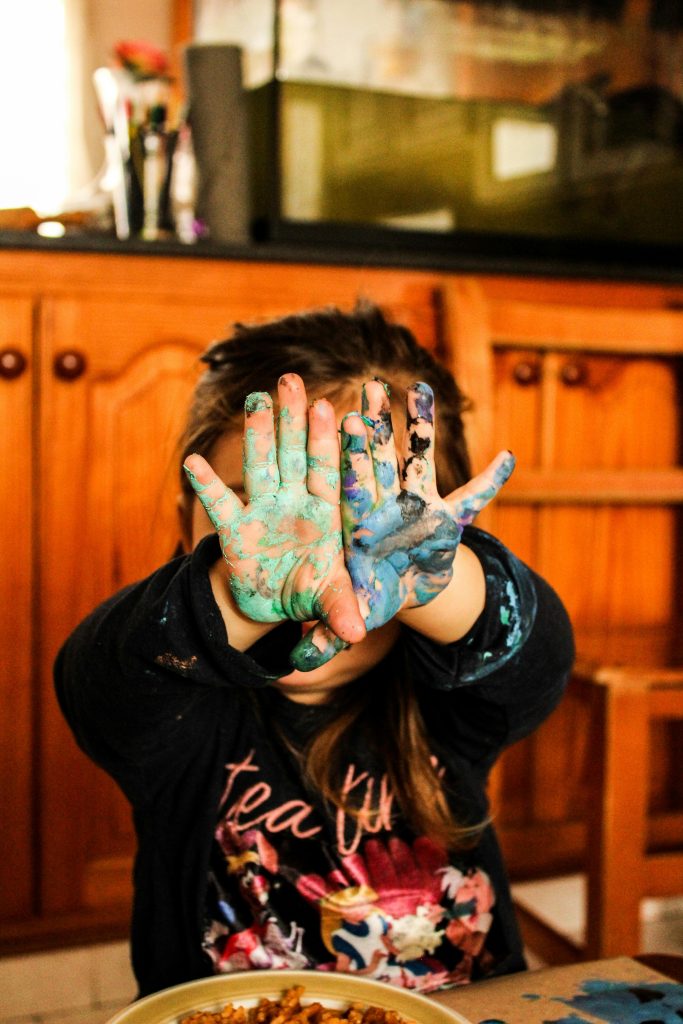 A child shows colorful painted hands during a fun and messy indoor art project.