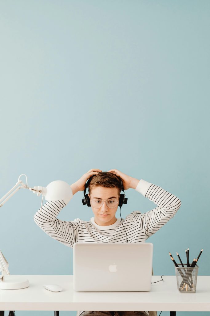 A young man wearing headphones sits at a desk working on a laptop in a bright, modern room.